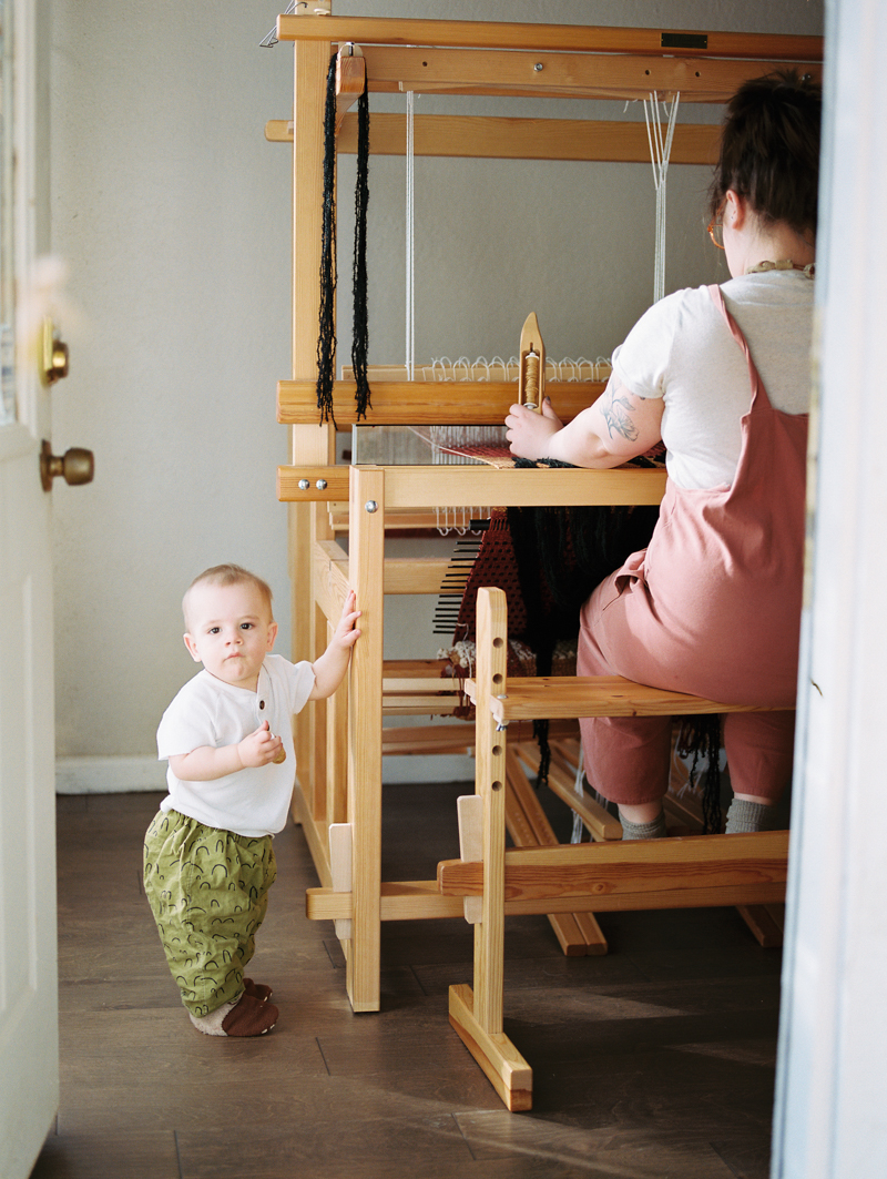 mother working on loom with child standing next to her