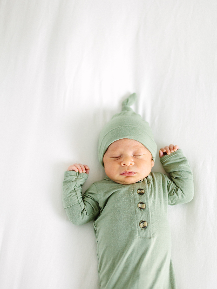newborn in green outfit laying on bed