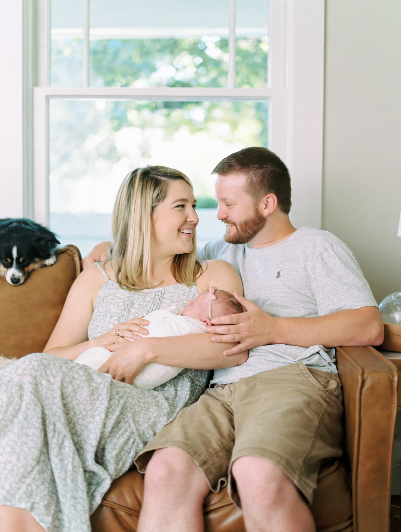 husband and wife smiling at each other while holding newborn