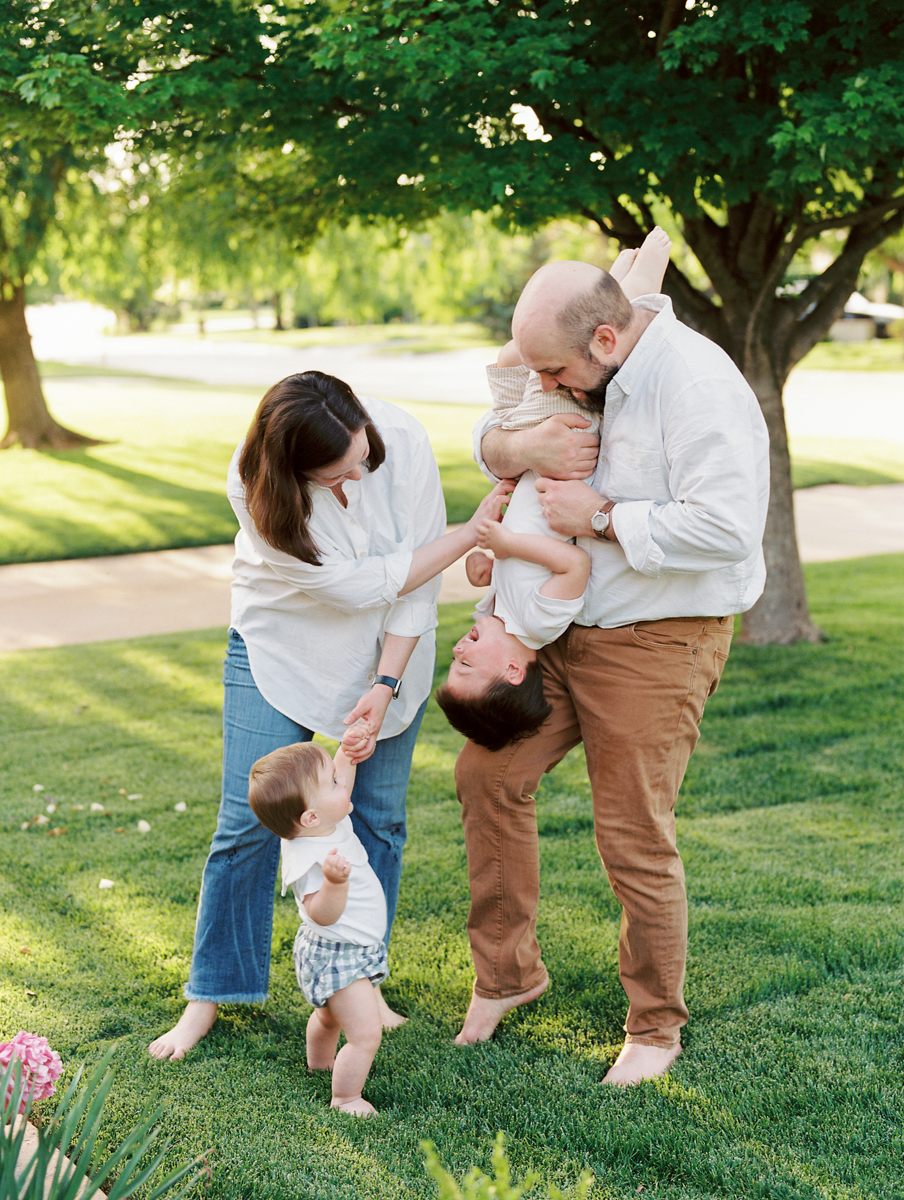 playful portrait of an okc family in their yard. mom and dad tickling son with little brother standing next to mom