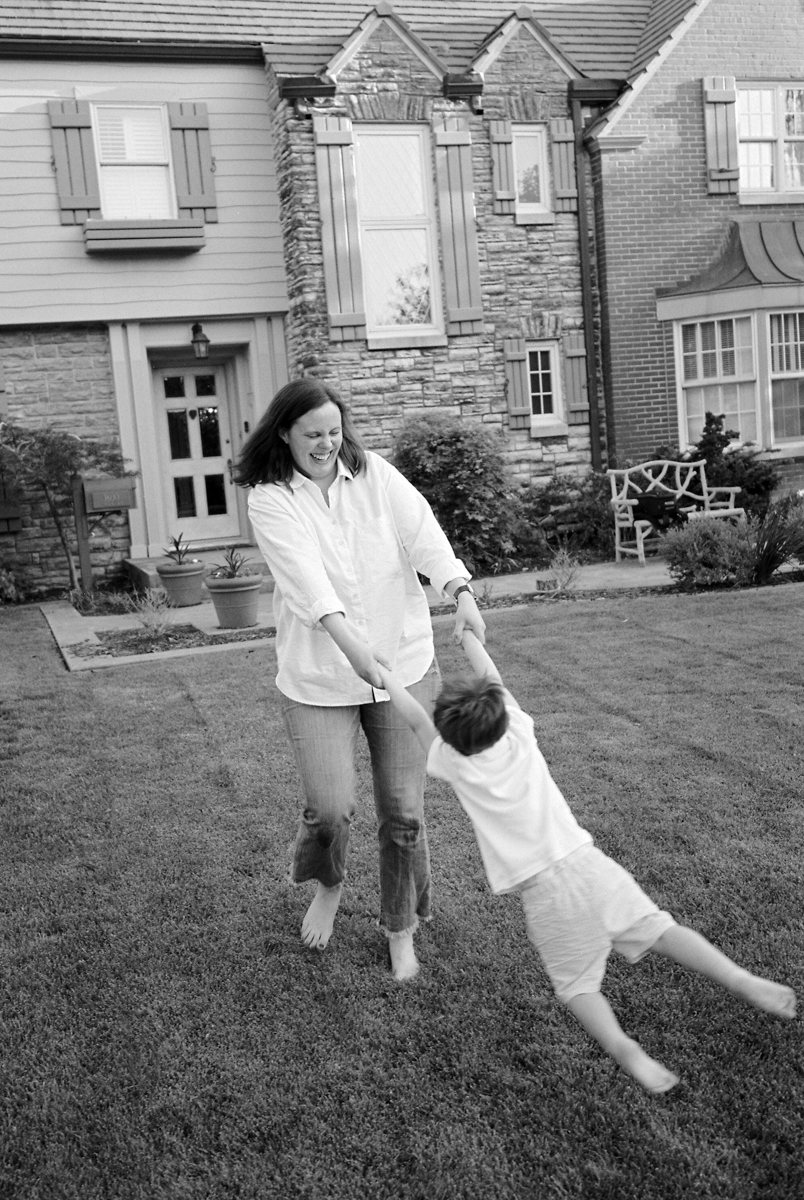 black and white photo of mom swinging son around front yard