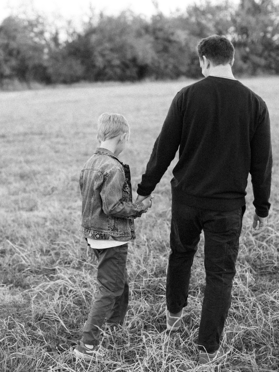 black and white photo of a father and son holding hands and walking through a field