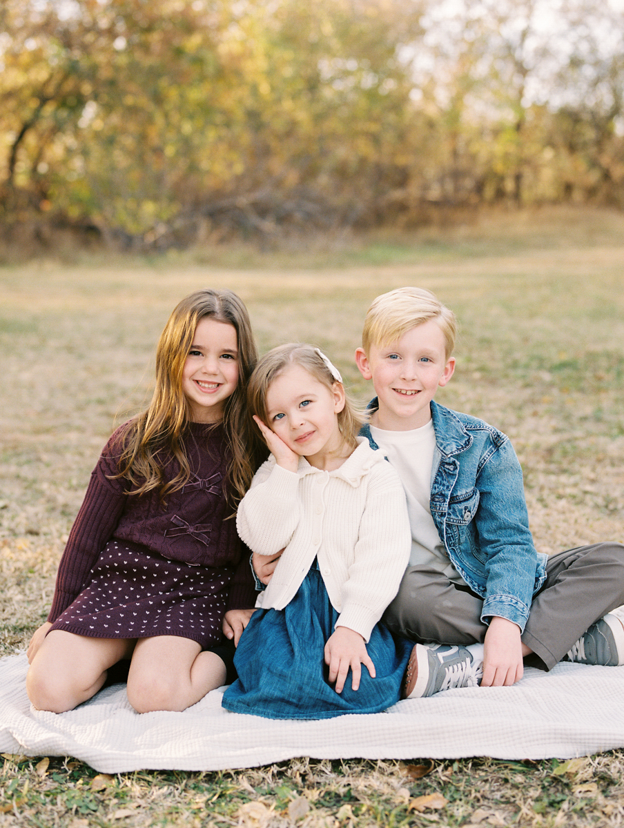 a portrait of three young children sitting on the blanket in okc