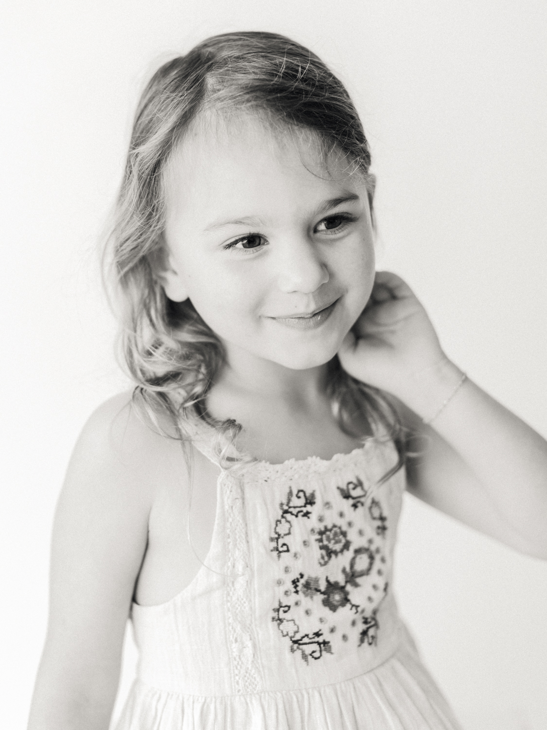 black and white portrait of young girl sweeping hair behind ear and smiling