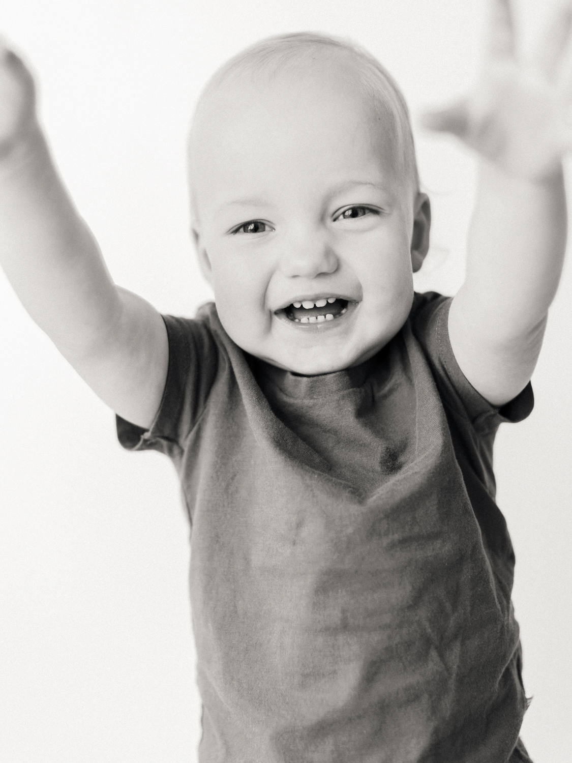 black and white portrait of toddler smiling and raising arms above head