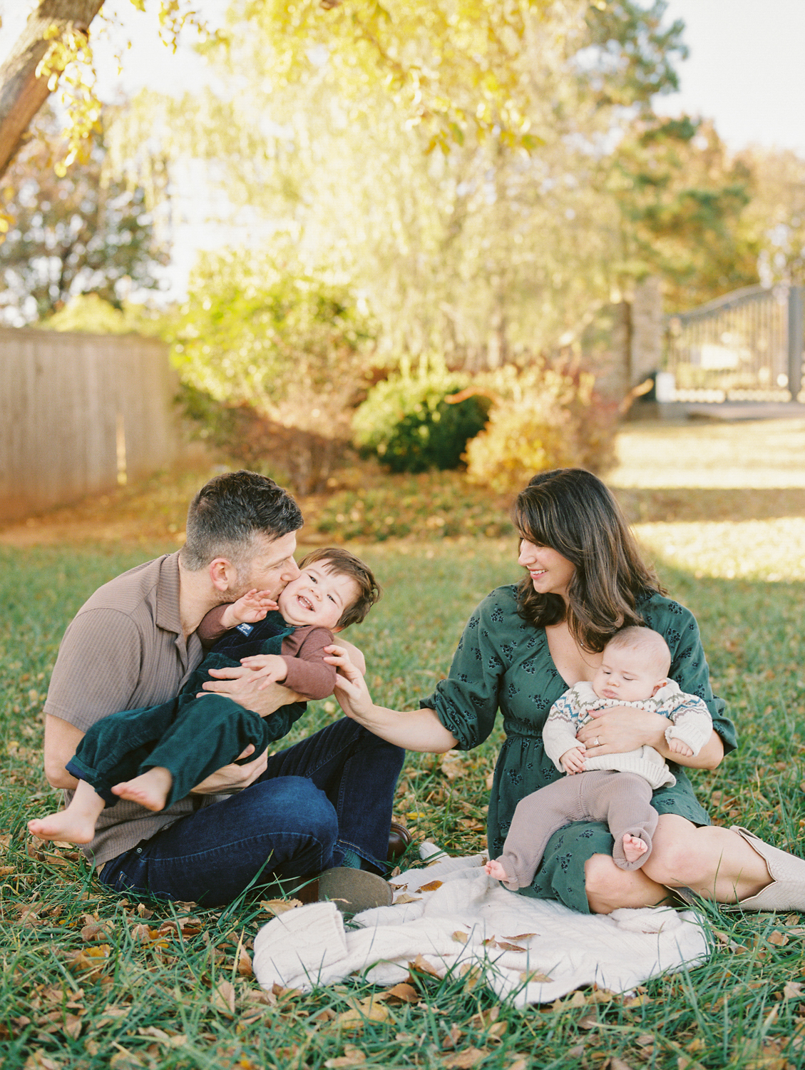 family in a fall setting, tickling their young son, with their new baby sitting in mom's lap